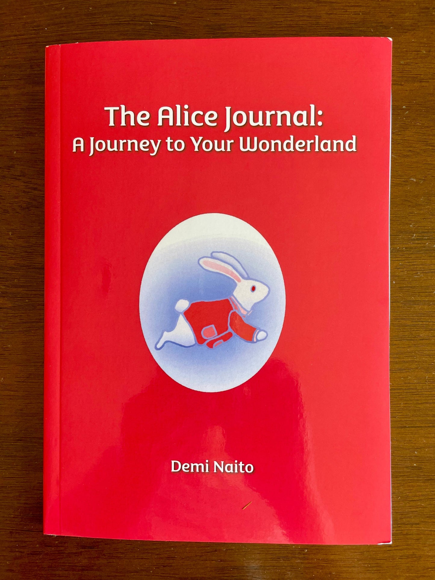 The softcover version of 'The Alice Journal: A Journey to Your Wonderland' with a rabbit illustration on a wooden surface