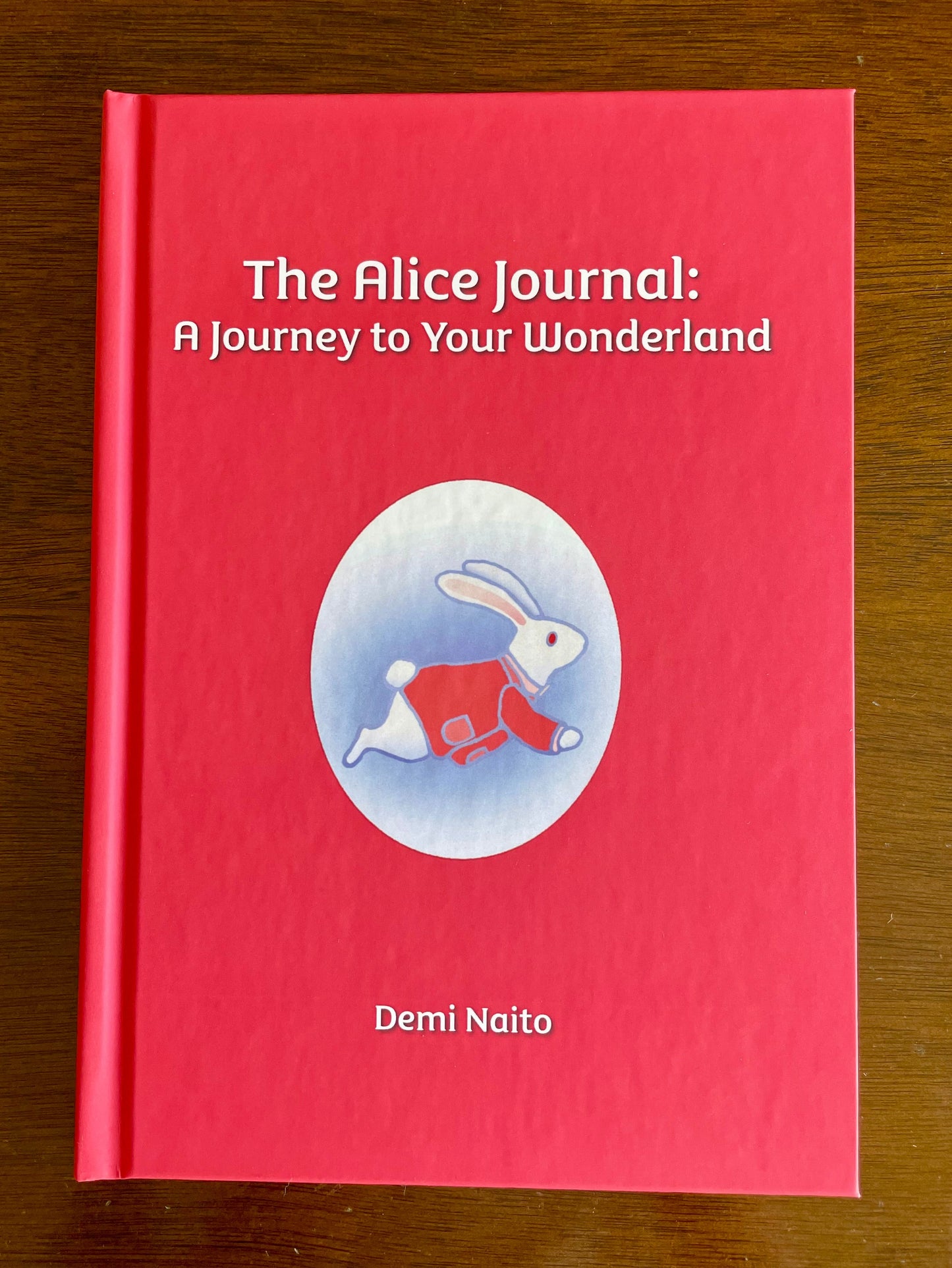 The hardcover version of  'The Alice Journal: A Journey to Your Wonderland' by Demi Naito on a wooden surface