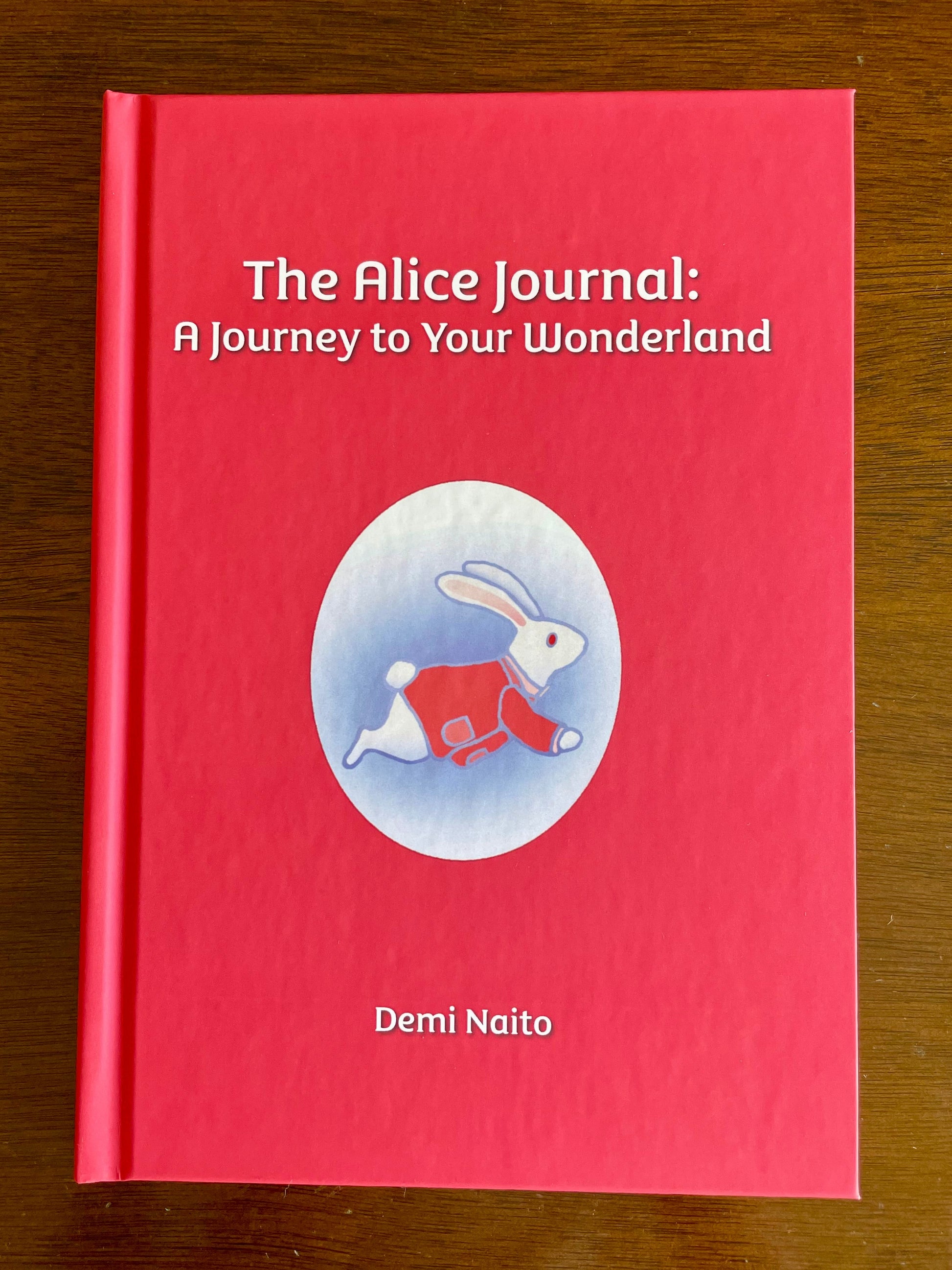 The hardcover version of  'The Alice Journal: A Journey to Your Wonderland' by Demi Naito on a wooden surface