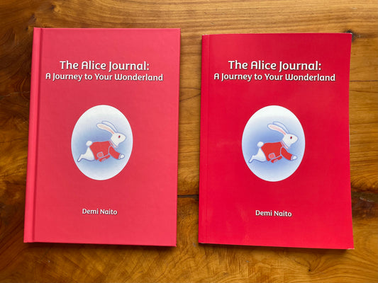Two softcover and hardcover versions of 'The Alice Journal: A Journey to Your Wonderland' by Demi Naito on a wooden surface.