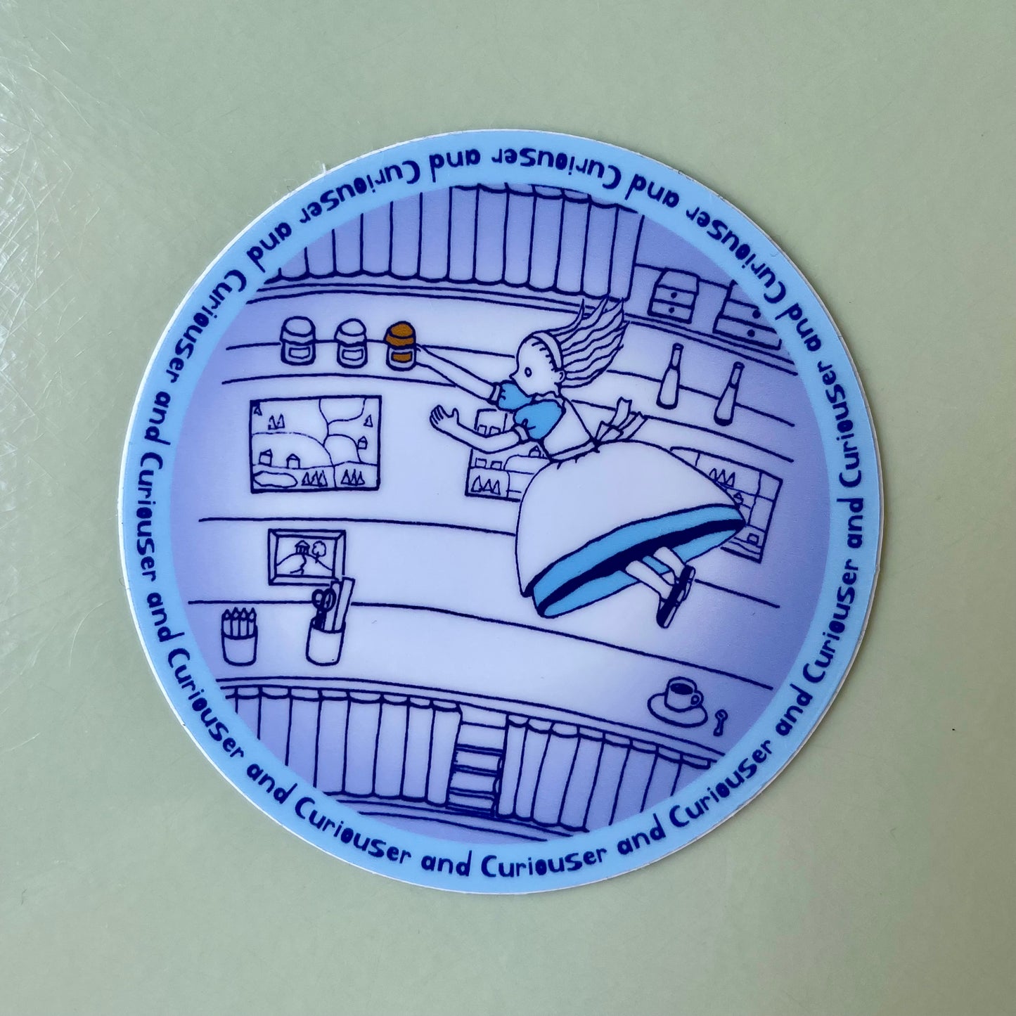 Circular sticker with a blue line drawing of Alice falling into the well