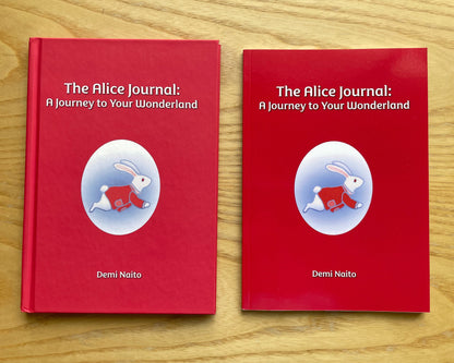 Two copies of the book 'The Alice Journal: A Journey to Your Wonderland' by Demi Naito, featuring red covers with a white rabbit illustration, displayed side-by-side on a light wood background.