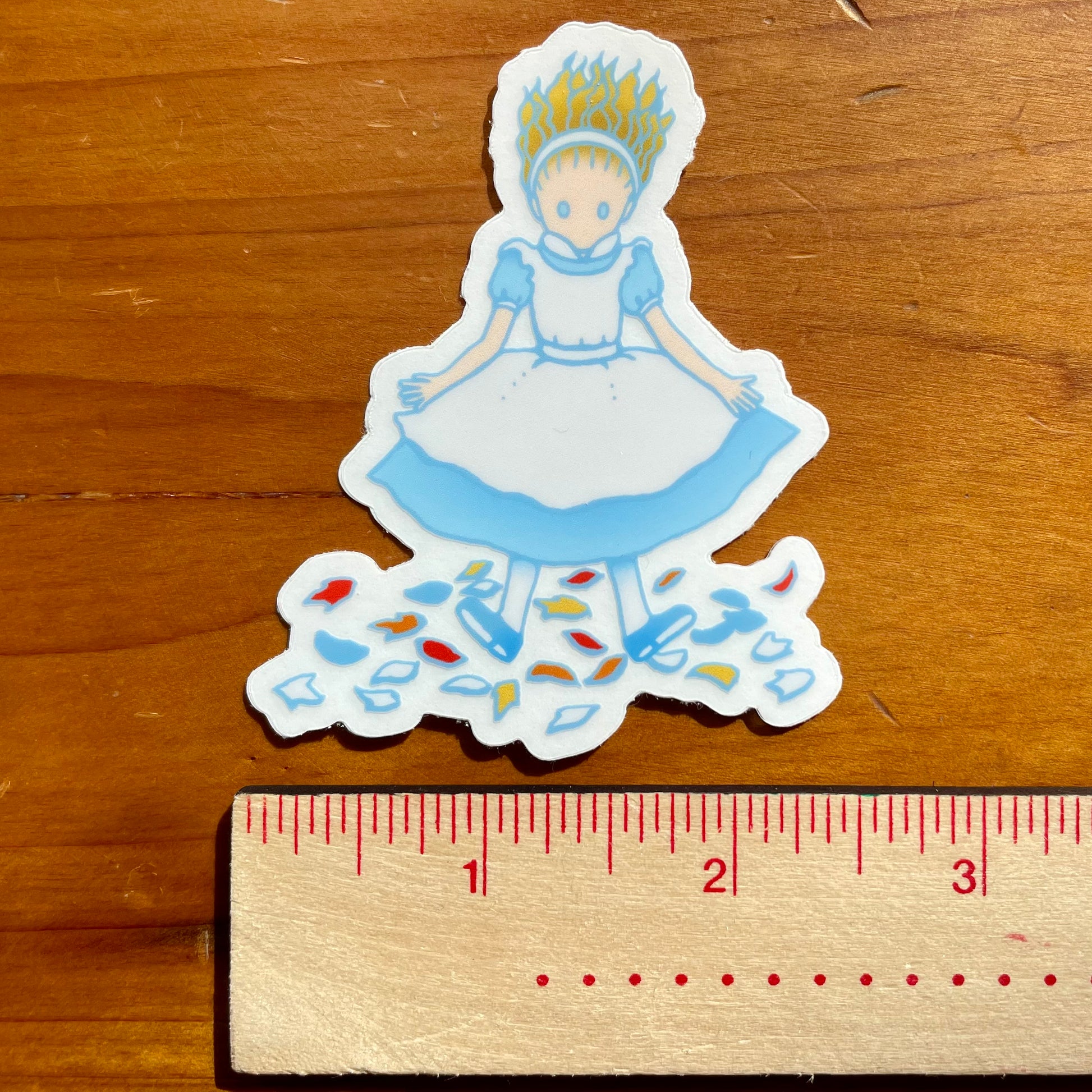 Sticker of Alice landing on a wooden surface with a ruler for scale.