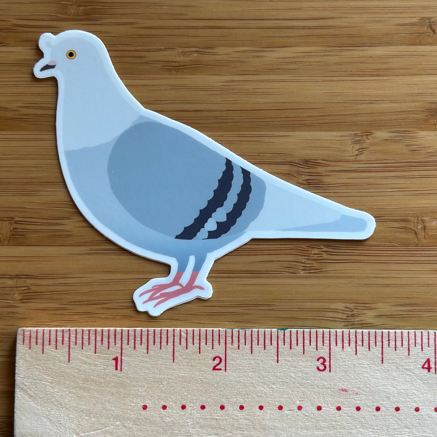 Sticker of a pigeon next to a ruler on a wooden surface