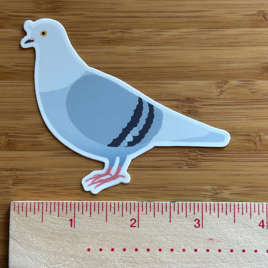 Sticker of a pigeon next to a ruler on a wooden surface