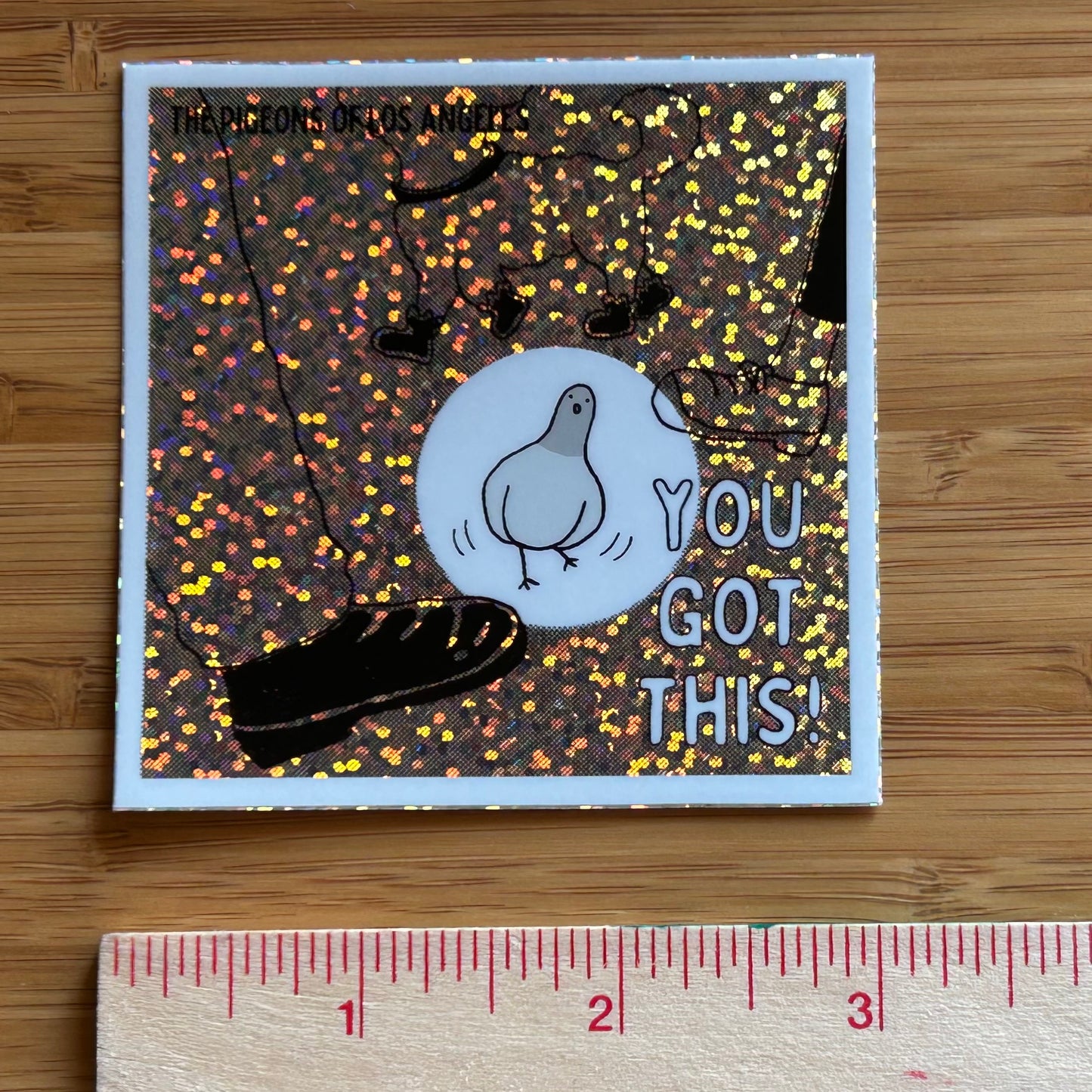 Square sticker with a comic pigeon avoiding feet and 'You Got This' text on a glittery, multi-colored background.