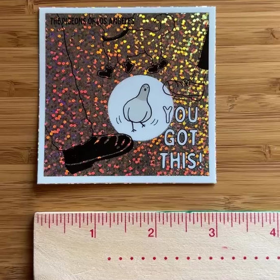 Video of square sticker with a comic pigeon avoiding feet and 'You Got This' text on a glittery, multi-colored background.